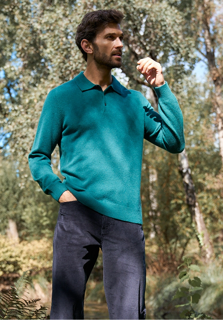 Man wearing a teal cashmere polo jumper and navy trousers outdoors