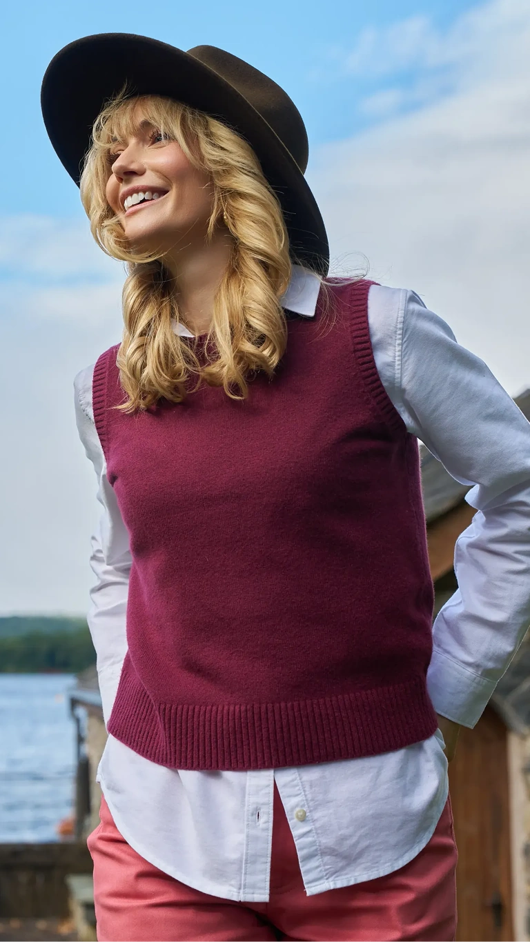 Woman wearing a burgundy sweater vest, white shirt and hat outdoors