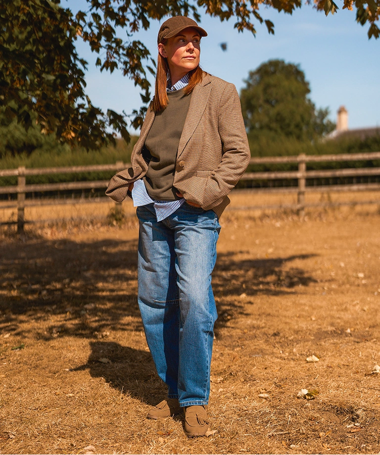 Eddie wearing a herringbone blazer, sweater, and jeans  on a sunlit country path.