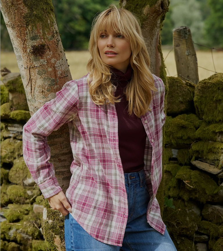 Woman wearing a pink checked shirt and jeans outdoors