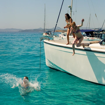 Three women having fun jumping from a sailing boat into the water