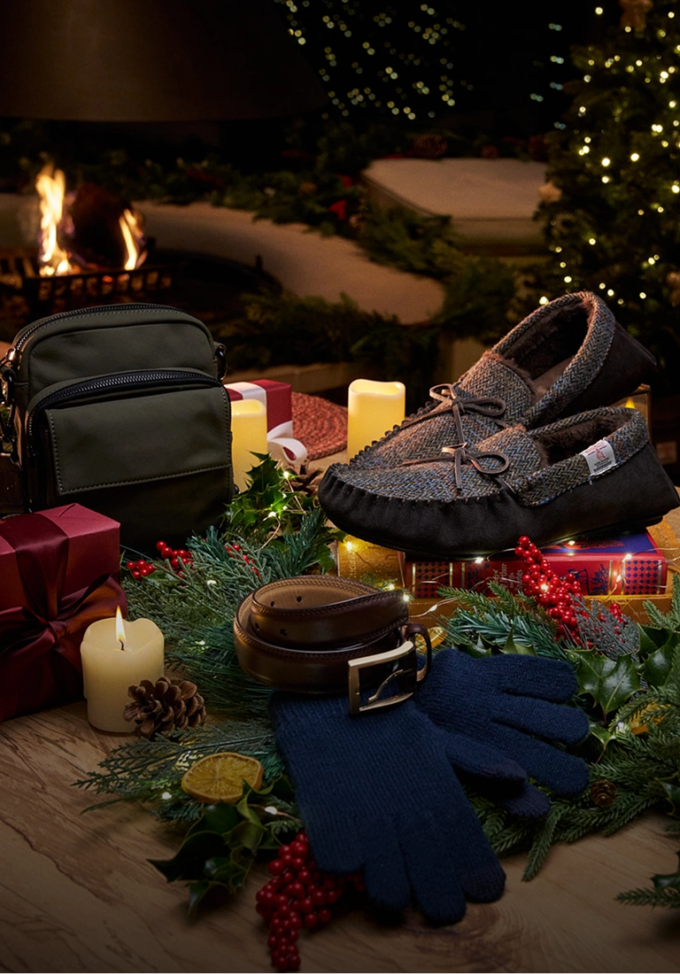 Christmas gifts including a bag, shoes, scarves and a blue beanie arranged with festive greenery and candles