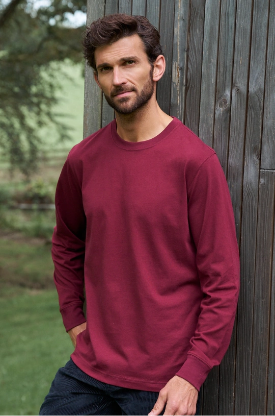 Man wearing a burgundy crew-neck sweatshirt and dark jeans outdoors