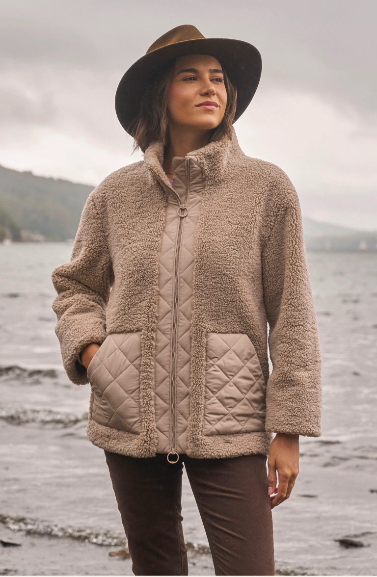 Woman wearing a quilted fleece jacket and wide-brimmed hat by the water
