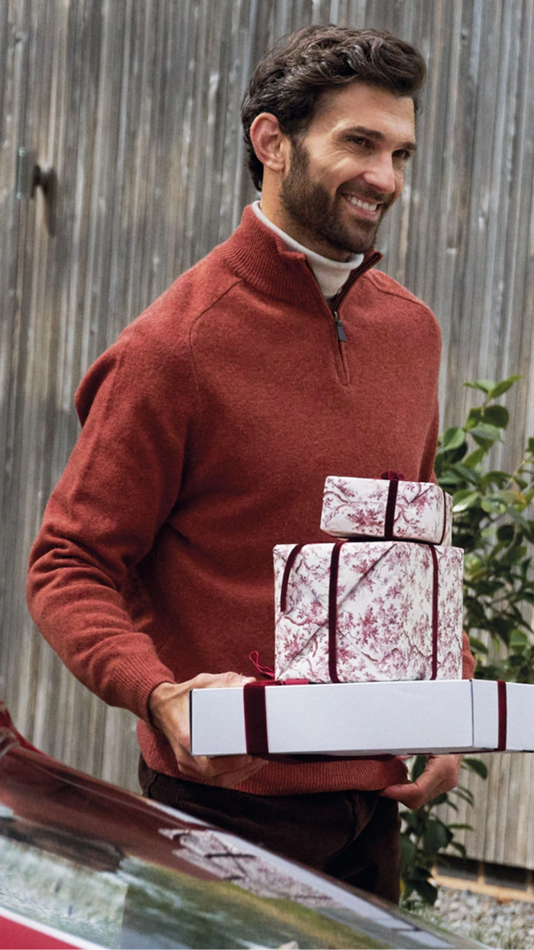 Man wearing a red quarter-zip jumper, holding wrapped Christmas gifts outdoors